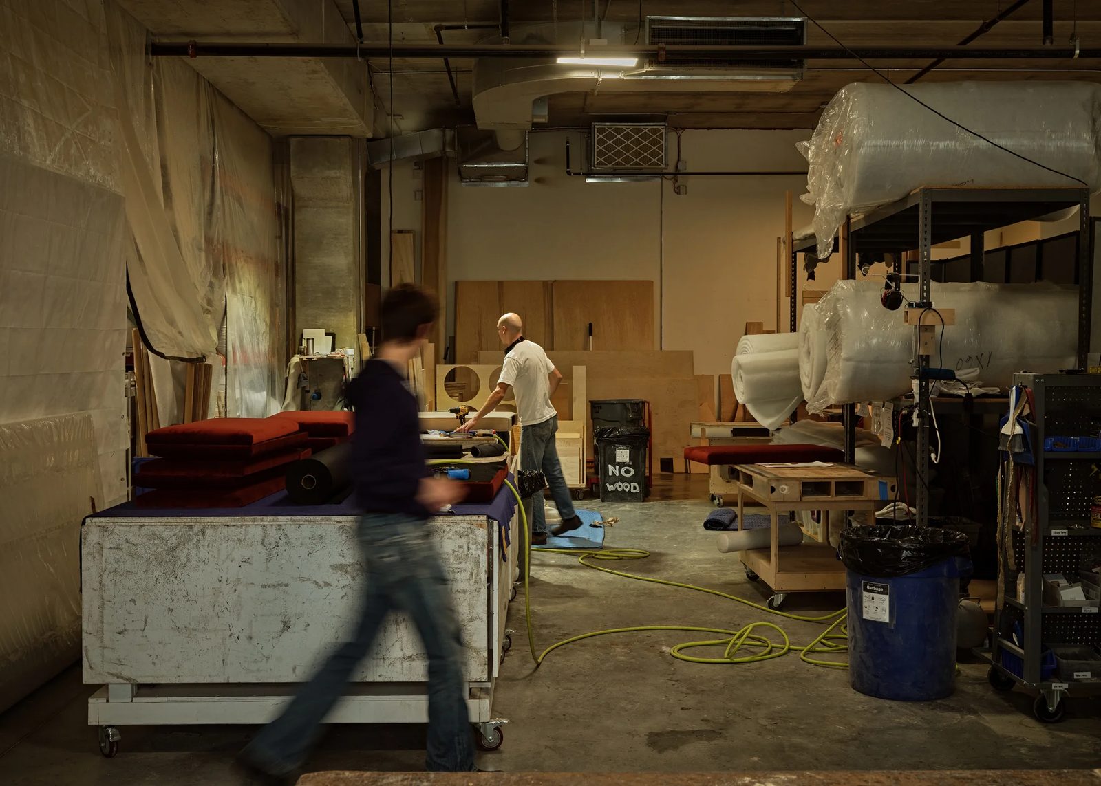 The Stitchroom workroom in the Brooklyn Navy Yard, with upholstered cushions on a cutting table, rolls of foam on shelving, and makers at work